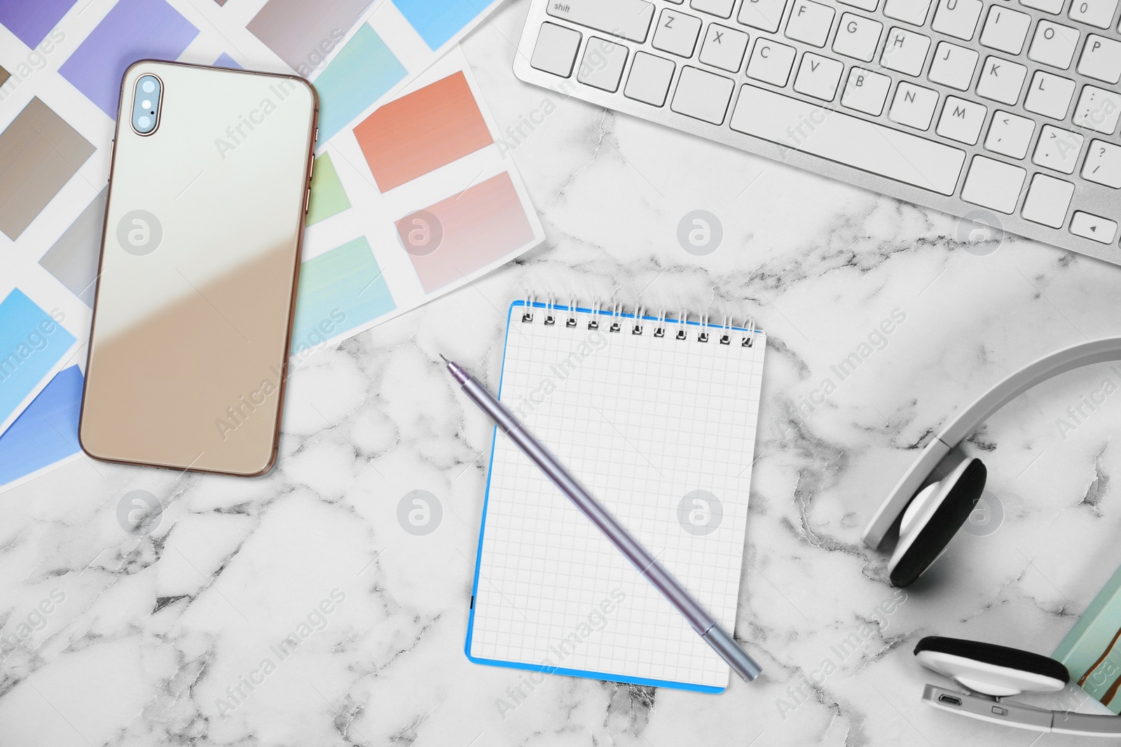 Photo of Flat lay composition with notebook, phone and color palettes on white marble table. Designer's workplace