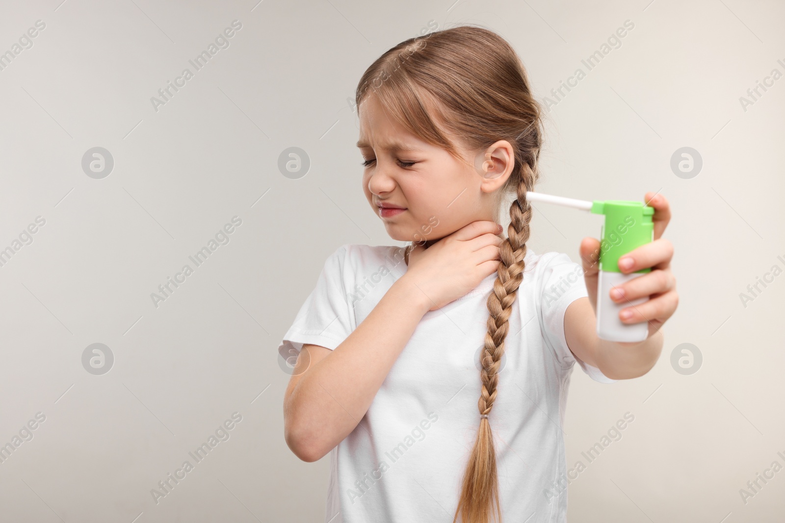 Photo of Little girl holding throat spray on light grey background. Space for text