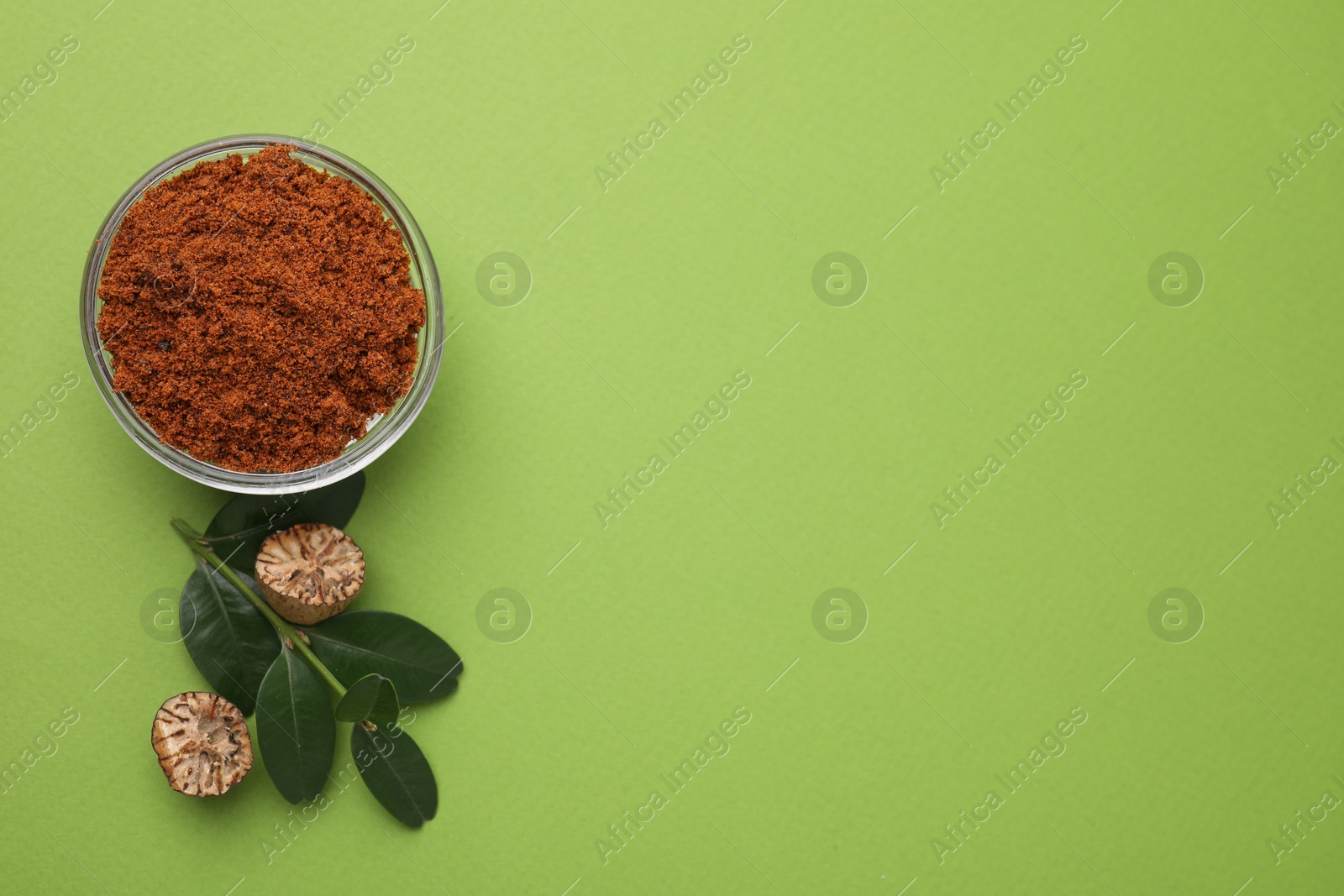 Photo of Nutmeg powder in bowl, halves of seed and branch on light green background, flat lay. Space for text