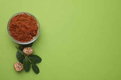 Nutmeg powder in bowl, halves of seed and branch on light green background, flat lay. Space for text