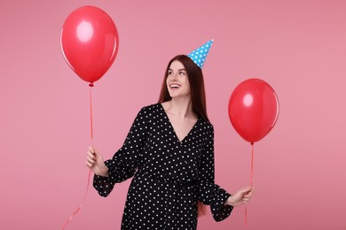 Happy woman in party hat with balloons on pink background