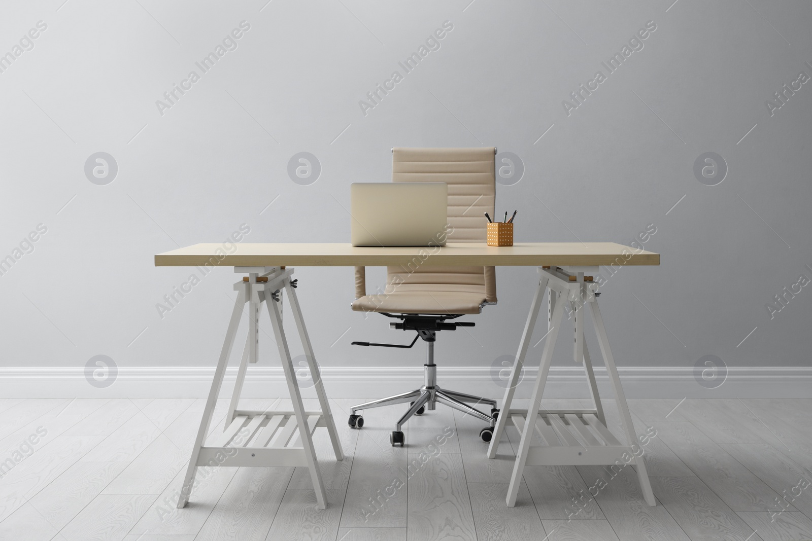 Photo of Stylish workplace with laptop and comfortable armchair near light wall indoors. Interior design