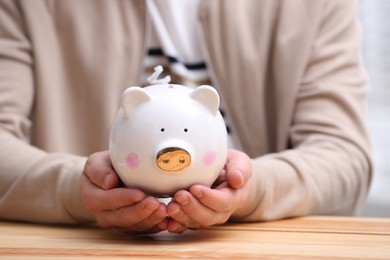 Man with piggy bank at wooden table, closeup