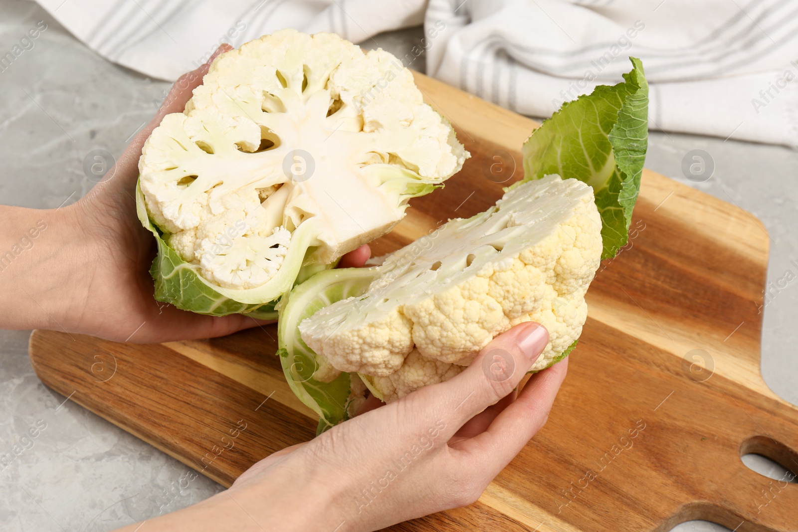 Photo of Woman with halves of fresh cauliflower at light grey table, closeup