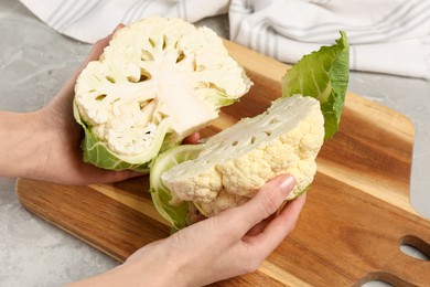 Woman with halves of fresh cauliflower at light grey table, closeup