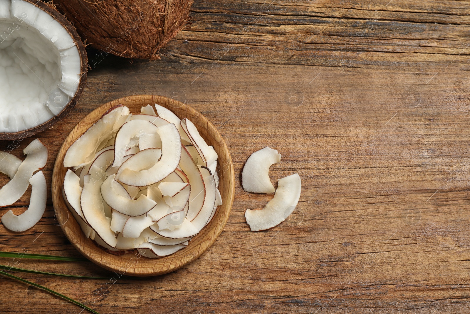 Photo of Tasty coconut chips on wooden table, flat lay. Space for text