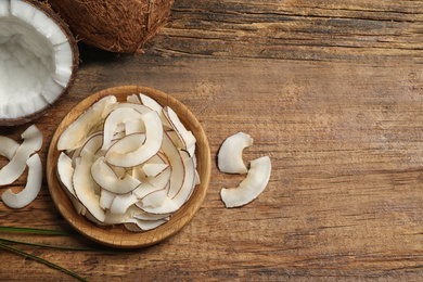 Tasty coconut chips on wooden table, flat lay. Space for text