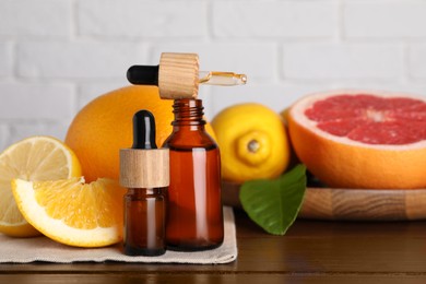 Photo of Bottles of essential oils with different citrus fruits and leaf on wooden table against white brick wall, closeup