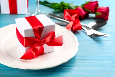 Photo of Beautiful table setting with gift box on light blue wooden background, closeup. Valentine's Day dinner