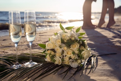 Photo of Beautiful wedding bouquet, glasses of champagne and couple on sandy beach
