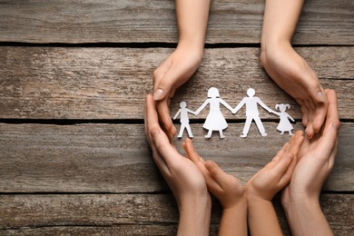 Parents and child protecting paper cutout of family at wooden table, top view. Space for text