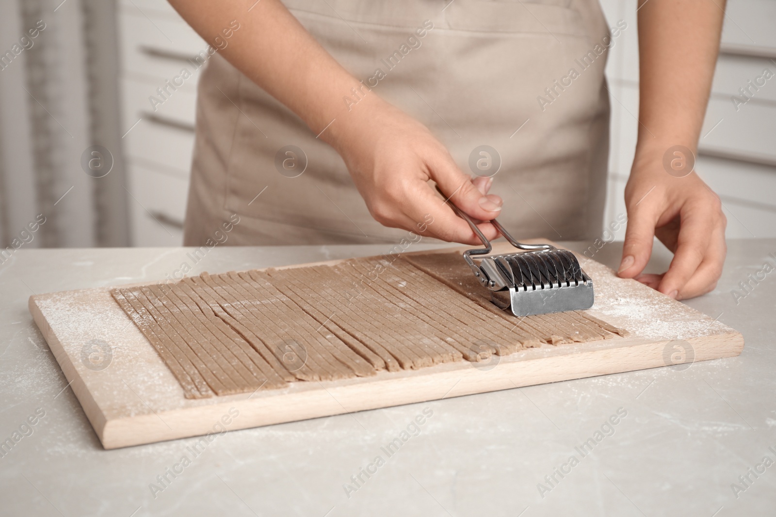 Photo of Woman making soba (buckwheat noodles) at light marble table, closeup