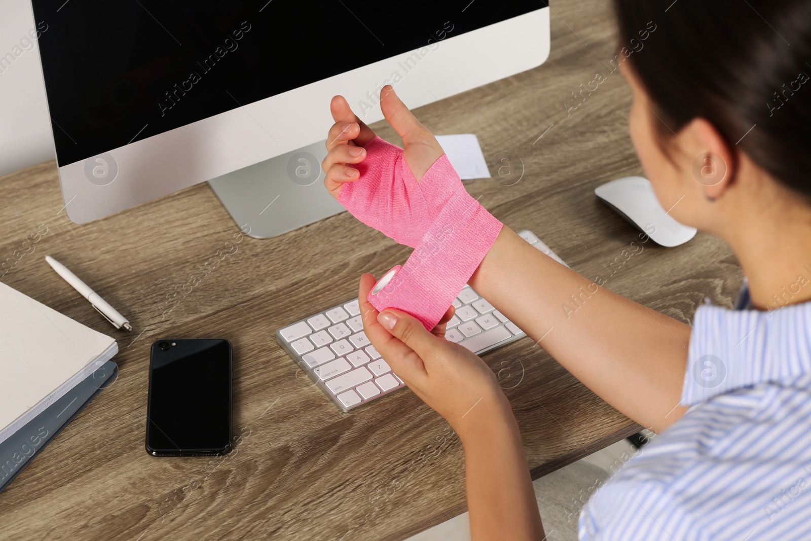 Photo of Young woman applying medical bandage onto hand at workplace, closeup