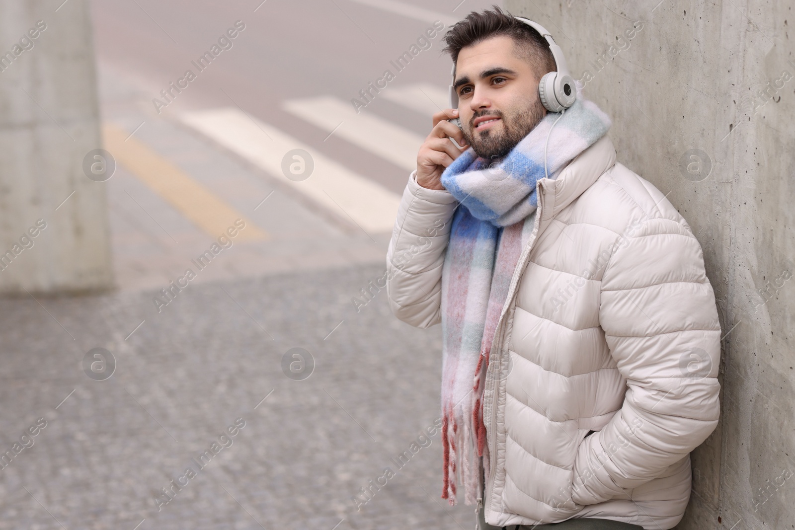 Photo of Smiling man in warm scarf and headphones on city street. Space for text