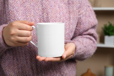 Photo of Woman holding white mug at home, closeup. Mockup for design