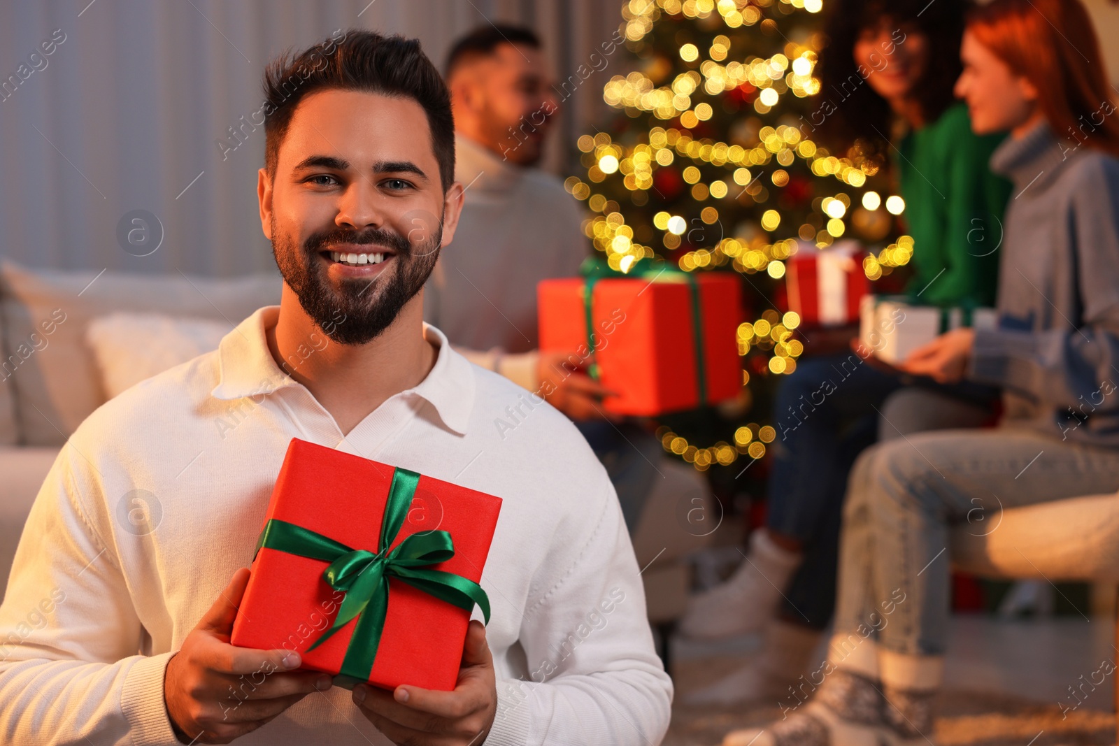 Photo of Christmas celebration in circle of friends. Happy young man with gift box at home, selective focus