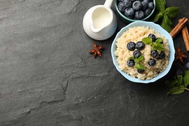 Photo of Flat lay composition with bowl of tasty quinoa porridge, blueberries and mint on black textured table. Space for text