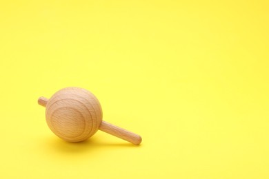 Photo of One wooden spinning top on yellow background, space for text. Toy whirligig