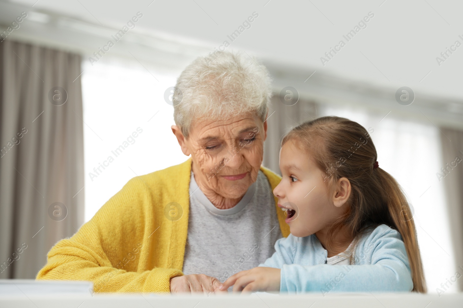 Photo of Cute girl and her grandmother reading book at home