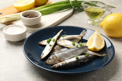 Photo of Fresh raw sprats, green onion, spices and cut lemon on grey table, closeup