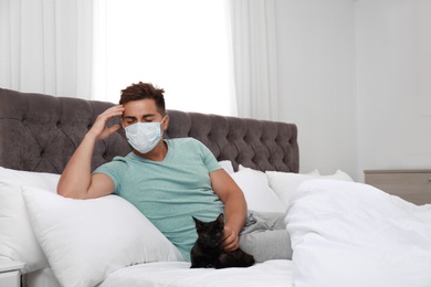 Young man with cat suffering from allergy in bedroom