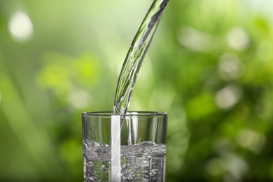 Photo of Pouring water into glass outdoors, closeup view