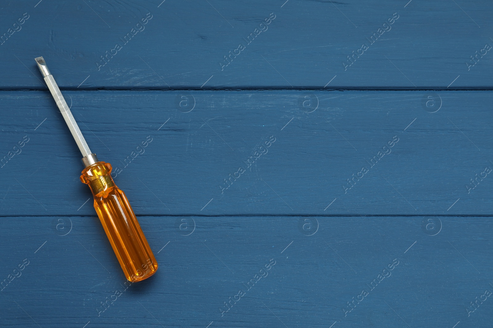 Photo of Screwdriver with orange handle on blue wooden table, top view. Space for text