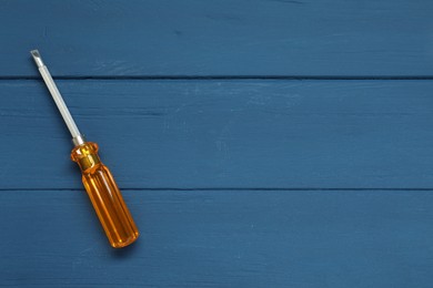 Screwdriver with orange handle on blue wooden table, top view. Space for text