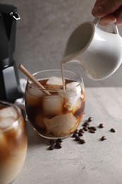 Photo of Woman pouring milk into glass with refreshing iced coffee at gray table, closeup