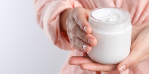 Woman holding jar of hand cream on white background, closeup view with space for text. Banner design