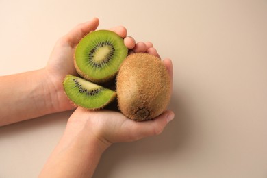 Photo of Woman holding cut and whole fresh kiwis on beige background, closeup