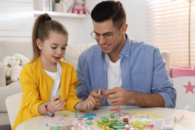 Photo of Happy father with his cute daughter making beaded jewelry at table in room