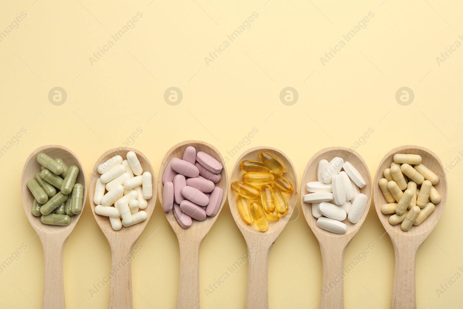 Photo of Different vitamin pills in spoons on pale yellow background, flat lay. Space for text