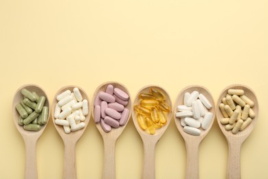 Photo of Different vitamin pills in spoons on pale yellow background, flat lay. Space for text