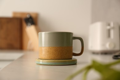 One ceramic mug with coaster on light countertop in kitchen