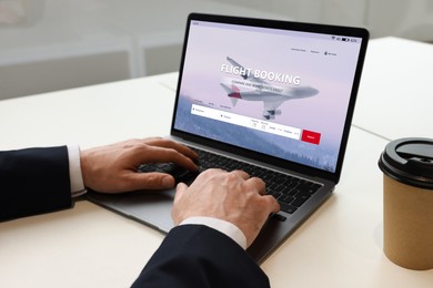 Image of Man using laptop to book flight at white table, closeup