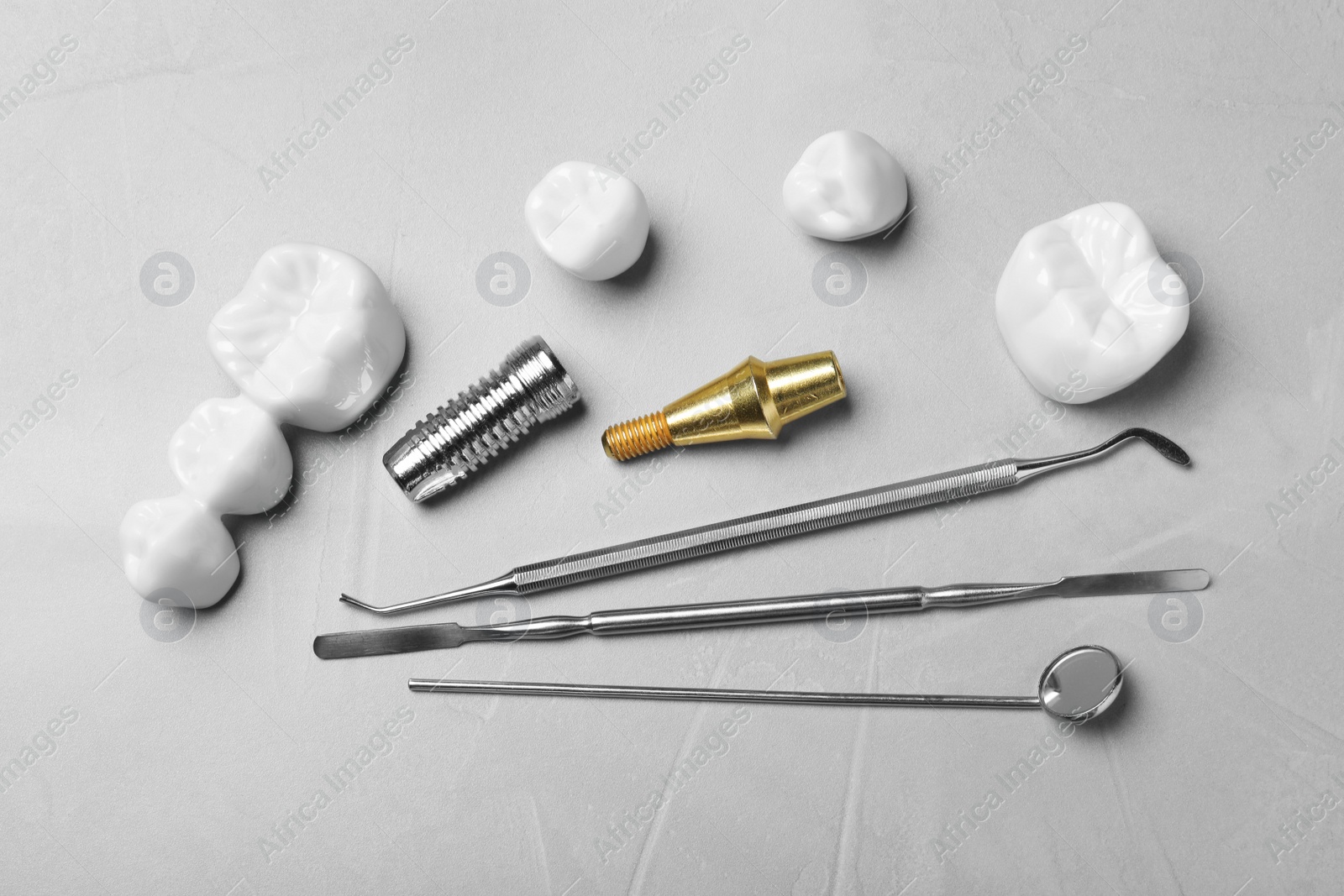 Photo of Post, abutment and different crowns of dental implant near medical tools on grey table, flat lay