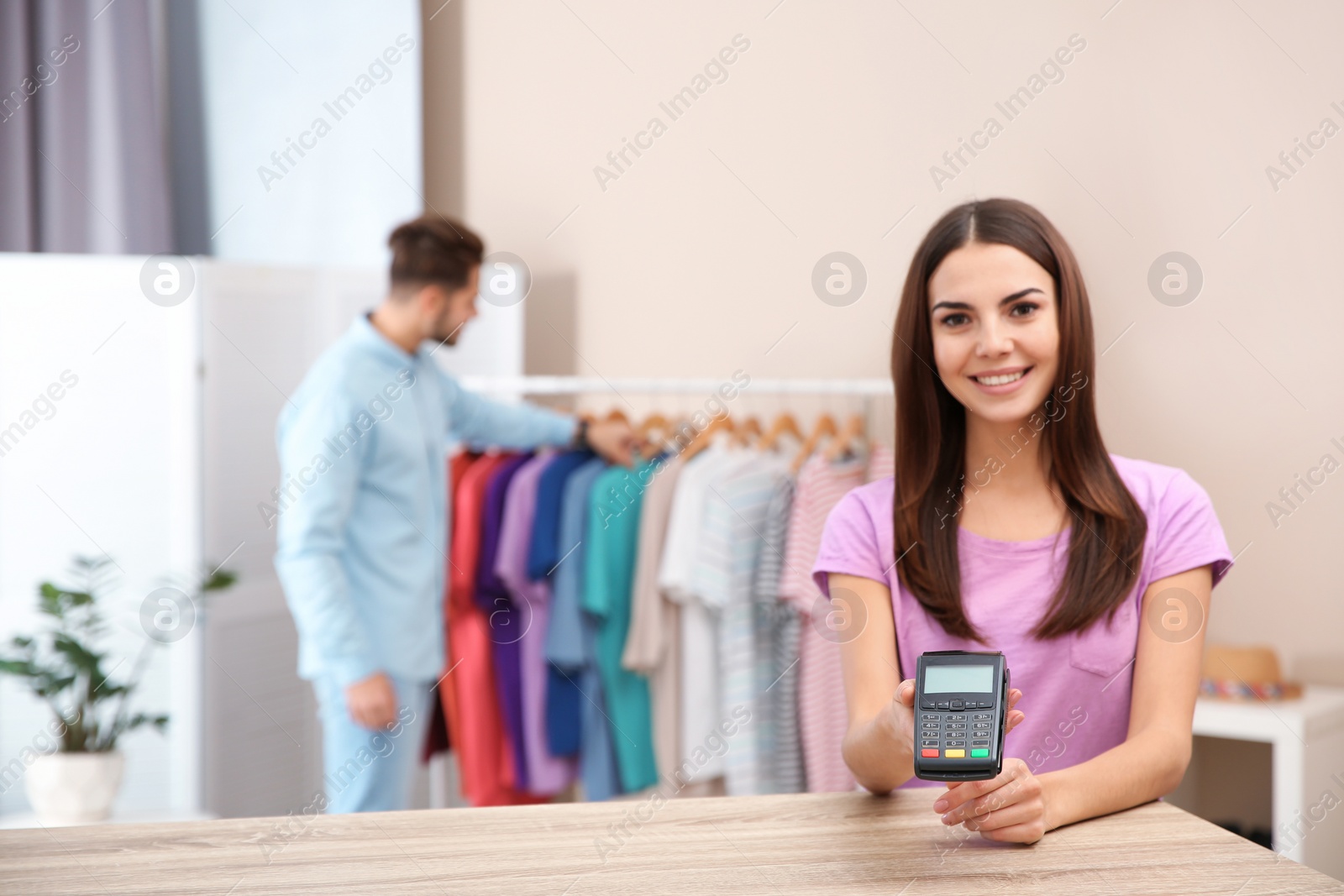 Photo of Female shop assistant with payment terminal at counter. Space for text