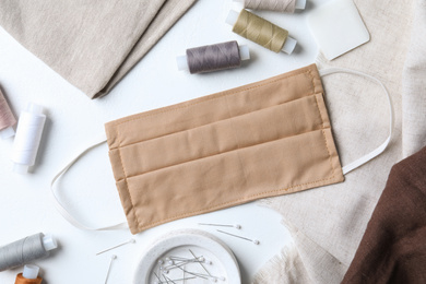 Homemade protective mask and sewing accessories on white background, flat lay