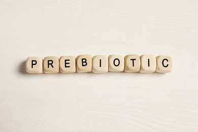 Word Prebiotic made of cubes on white wooden table, flat lay