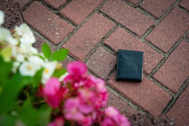 Photo of Black wallet on pavement outdoors, above view. Lost and found