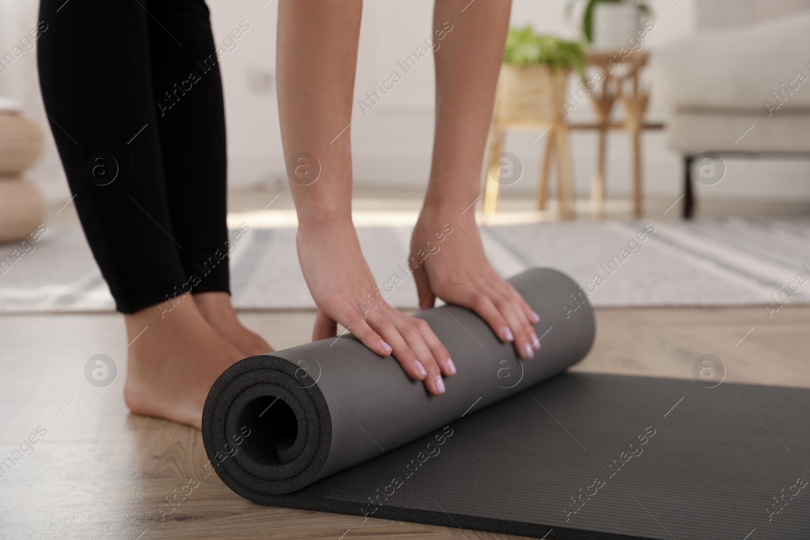 Photo of Woman unrolling yoga mat at home, closeup