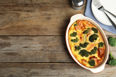 Tasty broccoli casserole in baking dish on wooden table, flat lay. Space for text