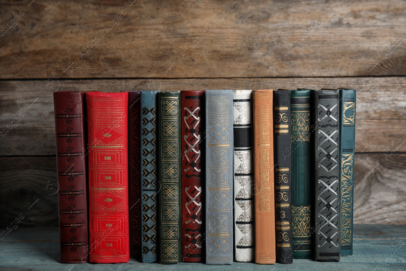 Photo of Stack of hardcover books on light blue table against wooden background