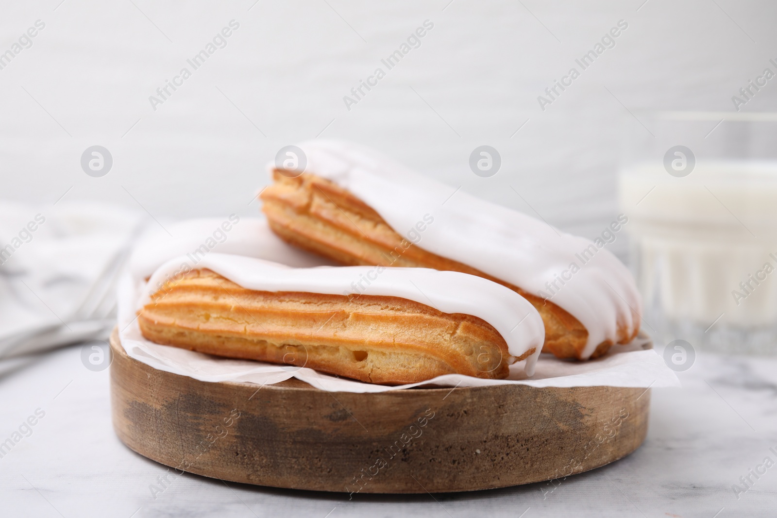 Photo of Delicious eclairs covered with glaze on white marble table, closeup