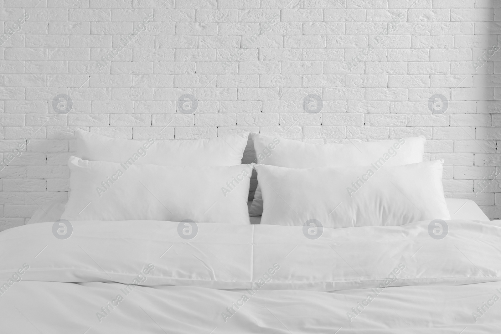 Photo of Large comfortable bed with pillows and blanket near white brick wall indoors. Stylish interior