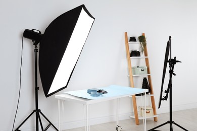 Professional lighting equipment near table with fashionable women's accessories in photo studio