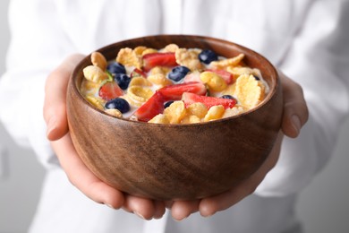 Photo of Woman holding bowl of crispy corn flakes with milk and berries, closeup
