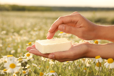Photo of Woman holding natural soap in chamomile field, closeup