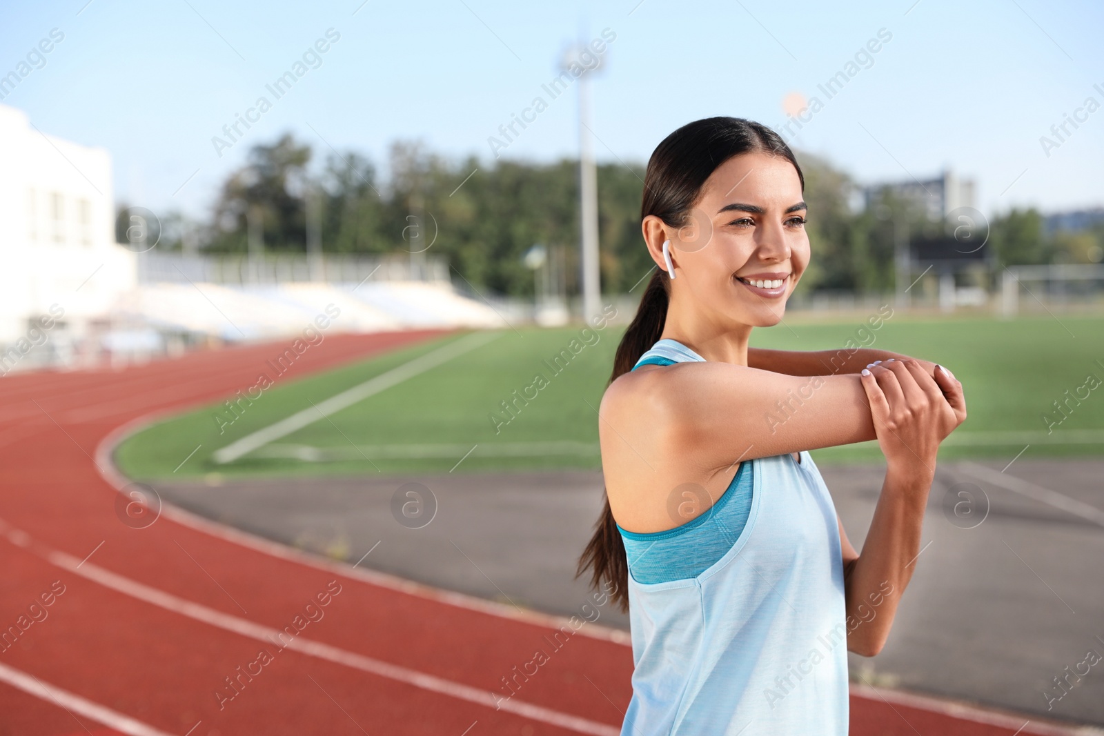 Photo of Young sportswoman with wireless earphones stretching at stadium